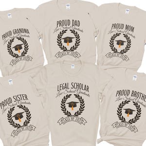 May include: Six beige t-shirts with black text and graphics. The shirts say "Proud Grandma", "Proud Dad", "Proud Mom", "Legal Scholar", "Proud Sister", and "Proud Brother". Each shirt has a laurel wreath with a graduation cap and the text "Law School Graduate" and "Class of 2025".