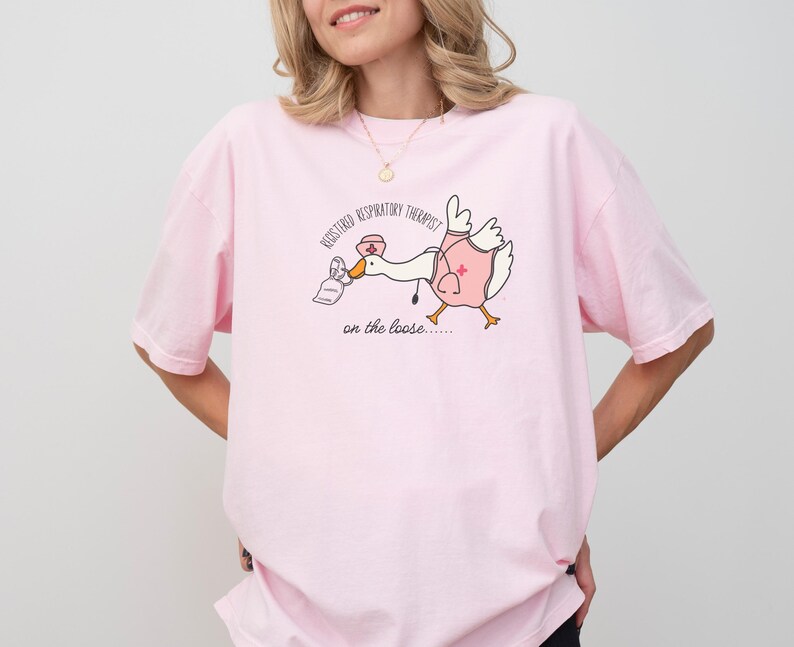May include: Pink t-shirt with a cartoon goose wearing a nurse's hat and holding a face mask. The text on the shirt reads "Registered Respiratory Therapist on the loose..."