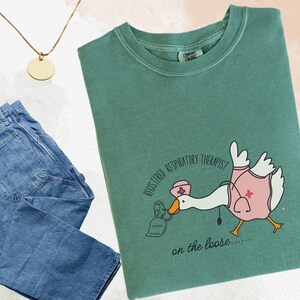 May include: A green t-shirt with a cartoon goose wearing a nurse's hat and holding a face mask. The text on the shirt reads "Registered Respiratory Therapist on the loose..."