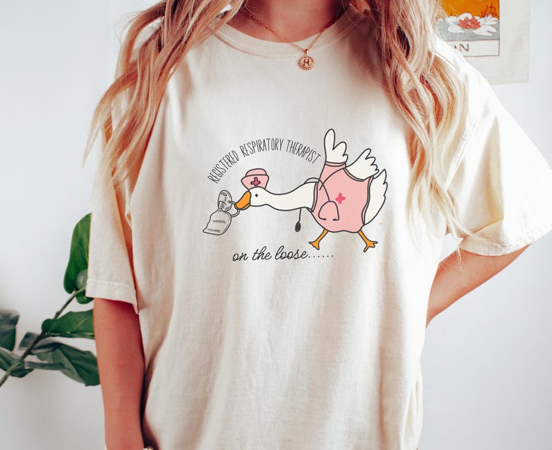 May include: A white t-shirt with a cartoon goose wearing a nurse's hat and holding a face mask. The text on the shirt reads "Registered Respiratory Therapist on the loose..."