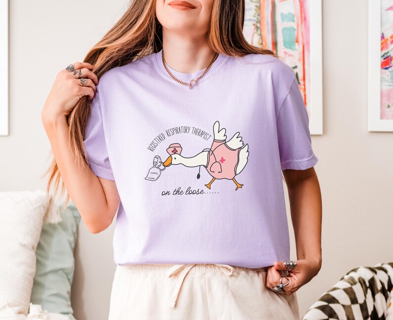 May include: A purple t-shirt with a cartoon goose wearing a nurse's hat and holding a nebulizer. The text on the shirt reads "Registered Respiratory Therapist on the loose..."