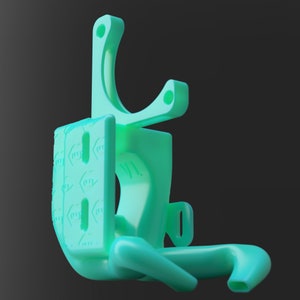 May include: A light green 3D-printed plastic object with a curved top, a rectangular base, and a curved arm. The base has a pattern of small, repeating symbols. The object appears to be a bracket or holder of some kind.