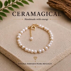 May include: A bracelet featuring white baroque pearls alternating with small gold-toned metal beads. The piece includes a gold-toned heart-shaped clasp and an adjustable chain extension with a single pearl at the end. Text reads CERAMAGICAL.