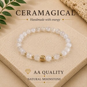 May include: A beaded bracelet made of translucent white natural moonstone spheres, accented with small gold-toned metal beads and a central textured gold-toned barrel bead. The text CERAMAGICAL, Handmade with energy, AA QUALITY, and NATURAL MOONSTONE is visible.