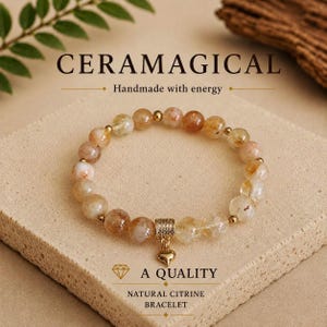 May include: A beaded bracelet featuring translucent, golden-yellow natural citrine stones interspersed with small gold-toned metal beads. A cylindrical gold-toned charm holder with a small dangling heart pendant is attached to the bracelet.