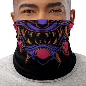 Puede incluir: Una máscara facial negra con un diseño colorido de la cara de un monstruo con dientes afilados y una nariz rosa.