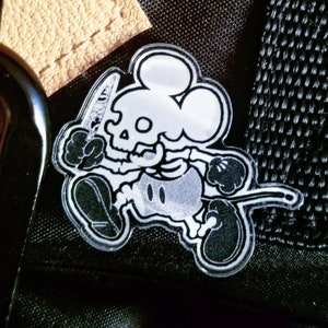 Puede incluir: Un parche de tela negro con un personaje de Mickey Mouse esqueleto blanco que sostiene un cuchillo.