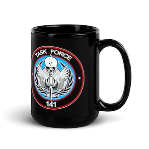 May include: Black ceramic mug featuring a circular emblem with a skull, wings, and a sword. The emblem is surrounded by the words "TASK FORCE" and "141". The design includes red, blue, white, and black colors.