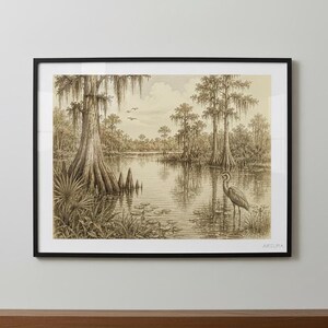 A framed pencil sketch of a wetland scene with a heron, cypress trees, and lily pads, displayed on a light wood surface against a dark gray wall.