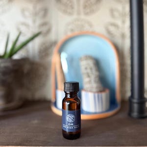 May include: A small brown glass bottle with a black cap and a blue label that says "OM Air Sign Oil".