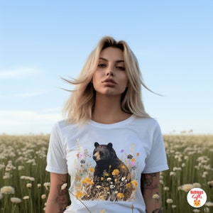 May include: A white t-shirt with a black bear surrounded by yellow, orange, and pink flowers. The bear is looking to the left of the image.