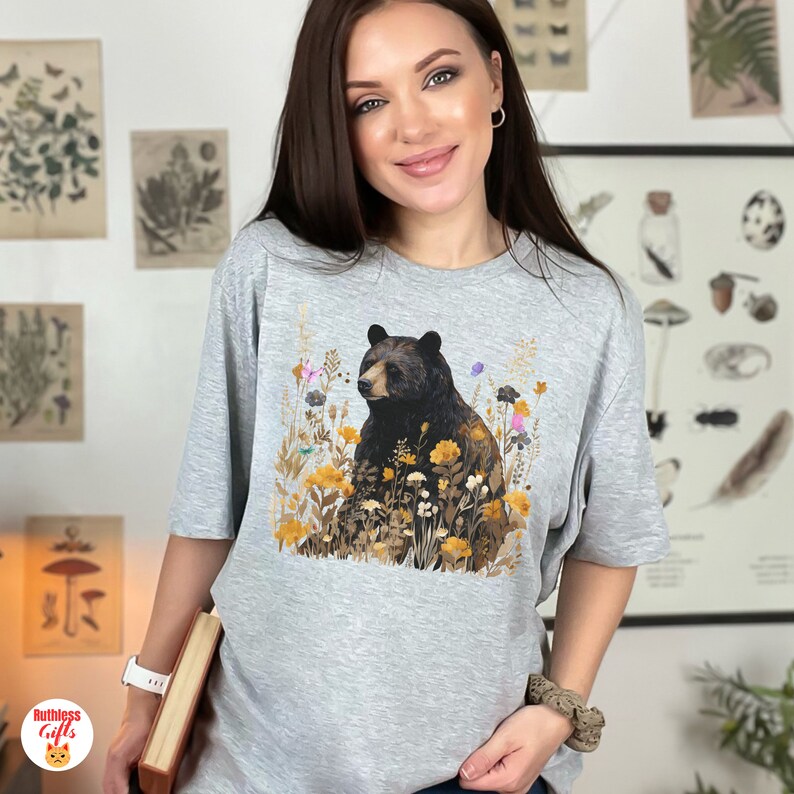 May include: A gray t-shirt with a black bear surrounded by yellow and orange flowers. The bear is sitting in a field of flowers.
