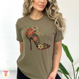 May include: A green t-shirt featuring a black high-heeled shoe with red soles and gold and red floral designs.