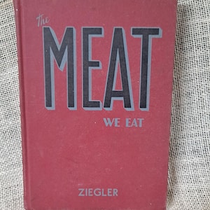 May include: A vintage book titled "The MEAT We Eat" with a red cover and black lettering. The author's name, Ziegler, is printed at the bottom. The book is set against a textured, neutral background.