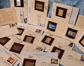 May include: A collection of First Day of Issue envelopes and commemorative stamps, featuring various designs and historical figures. The envelopes are cream-colored with a burgundy border, and some include the text "Women in Journalism". The background is a blue tie-dye fabric.