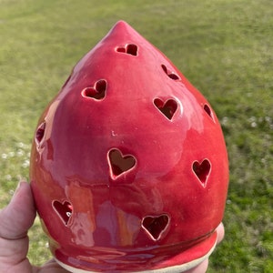 May include: A red ceramic candle holder shaped like a teardrop with heart-shaped cutouts.