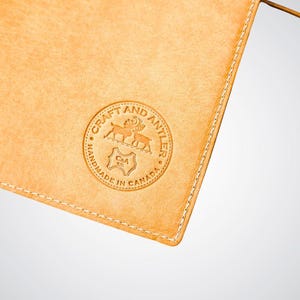 May include: A close-up of a light brown leather pouch with a stitched edge. The pouch has a circular logo embossed on the front that reads "Craft and Antler Handmade in Canada" with a stylized image of two deer and a C&A logo.