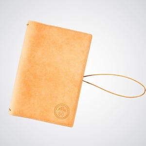 May include: A tan leather notebook cover with a brown leather strap and a circular logo that reads "Craft and Ancillary" with the text "Handcrafted in Canada" underneath.