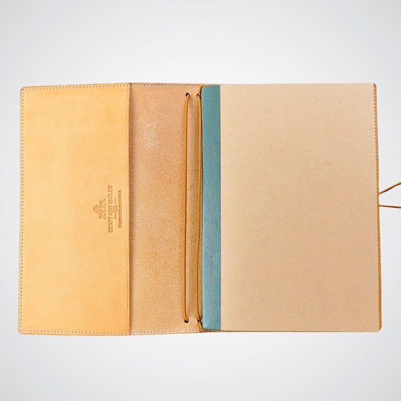 May include: A tan leather notebook cover with a blue ribbon and a brown leather strap. The cover has the text "L.L. Bean Craft and Leather Co. Established in Maine" printed on the front.