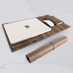 May include: A brown leather laptop desk pad with a rolled-up brown leather mouse pad. The laptop desk pad has a flap that can be folded over to protect the laptop. The mouse pad has the text "Crafted With Love" printed on it.