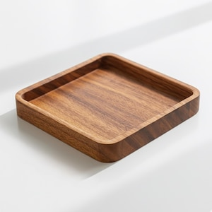 May include: A square wooden tray with a raised edge. The tray is made of a light brown wood with a visible grain pattern. The tray is empty and sits on a white surface.