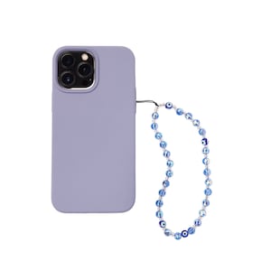 May include: A lavender silicone phone case with a beaded phone strap. The strap is made of blue and white beads with an evil eye design.