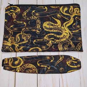 May include: A black zippered pouch and a matching wristlet with a gold and black snake print design.