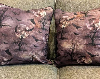 May include: Two decorative throw pillows with a spooky Halloween theme. The pillows feature a repeating pattern of full moons, bare trees, and flying bats against a dark purple background. The pillows have a black border.