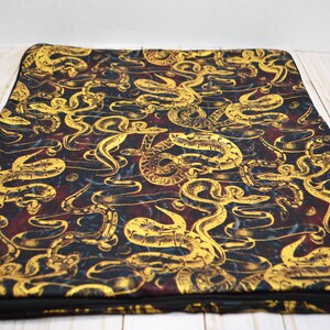 May include: A black and gold zippered pillow with a pattern of snakes. The snakes are in a swirling pattern and are a light gold color. The background is a dark black with hints of red.