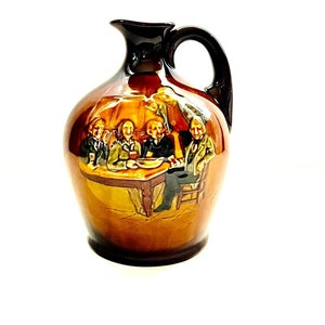 May include: A brown ceramic pitcher with a black handle and a scene of men drinking around a table. The pitcher has a brown glaze with a glossy finish.
