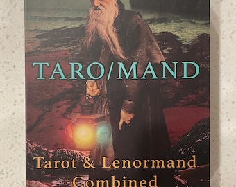 May include: A book cover with the title "TARO/MAND" and the subtitle "Tarot & Lenormand Combined" by Brad Ashlock. The cover features an illustration of a man in a turban holding a lantern, set against a coastal background with a lighthouse.