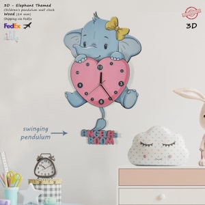 May include: A pink heart-shaped clock with a blue elephant holding it. The clock has a swinging pendulum and the words "ANGELA'S ROOM" are written below it. The clock is made of wood and is 24 mm thick.