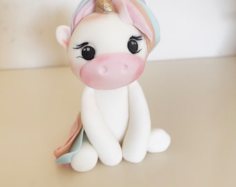 May include: A white unicorn figurine with a rainbow mane and tail. The unicorn has a gold horn and pink hooves.