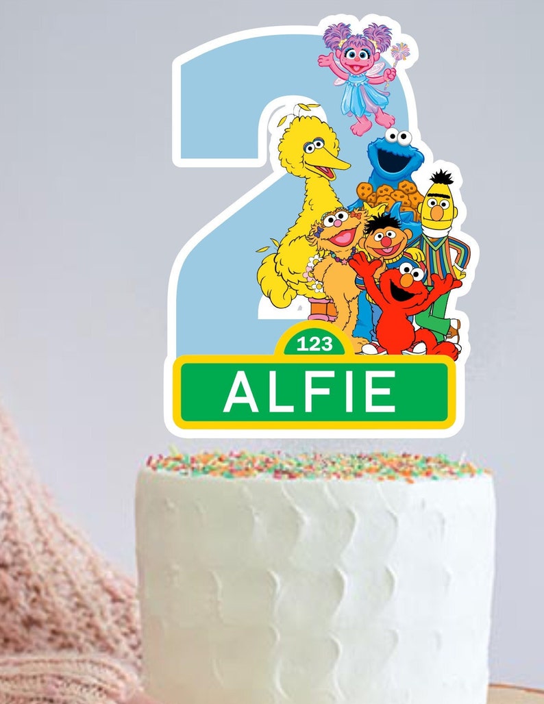 May include: A Sesame Street themed cake topper with a blue number 2, Big Bird, Elmo, Cookie Monster, and other characters. The topper also includes a green sign with the number 123 and the name Alfie.