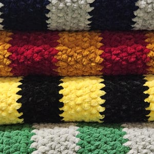 May include: Stack of four crocheted blankets in different color combinations. The blankets are striped with alternating colors of navy blue, gray, red, yellow, black, yellow, green, and gray.