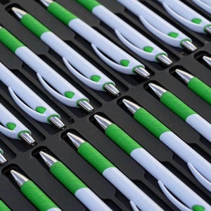 May include: A close-up view of a tray filled with white and green pens. The pens are arranged in rows and are all facing the same direction.