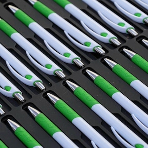 May include: A close-up view of a tray filled with white and green pens. The pens are arranged in rows and are all facing the same direction.