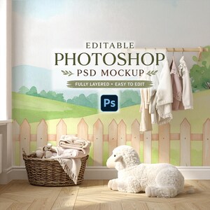 Op de afbeelding: Een mockup-scène voor een kinderkamer met een schapenknuffel, een rieten mand met dekens en knuffels en hangende babykleding. De muur heeft een geschilderde pastorale scène met een hek en groene heuvels. De tekst op de muur luidt "EDITABLE PHOTOSHOP PSD MOCKUP".
