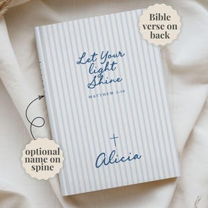 May include: A light blue and white striped notebook featuring the text Let Your Light Shine Matthew 5:16 and a cross symbol with the name Alicia. Text labels indicate Bible verse on back and optional name on spine.