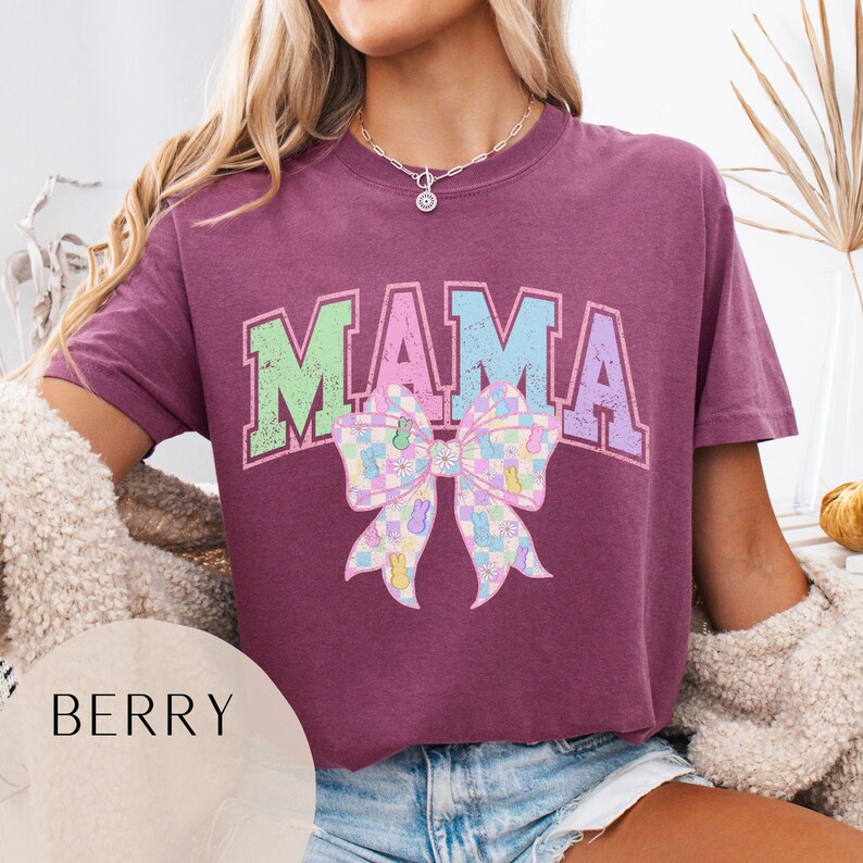 May include: Purple t-shirt with the word "MAMA" in colorful letters and a pastel checkered bow with bunny silhouettes.
