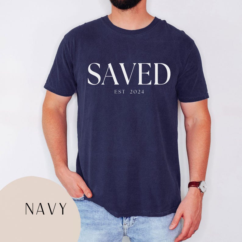 May include: A navy blue t-shirt with the word "SAVED" in white lettering and the text "EST 2024" underneath.