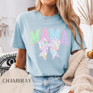 May include: A light blue t-shirt with the word "MAMA" in rainbow colors and a pastel checkered bow with a rhinestone in the center.