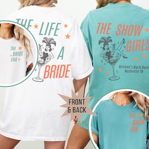 May include: White and teal t-shirts with text and graphics. The white shirt has "THE LIFE A BRIDE" and "THE BRIDE ERA" text. The teal shirt says "THE SHOW GIRLS" and "THE BACH ERA". Both shirts feature a woman in a martini glass.