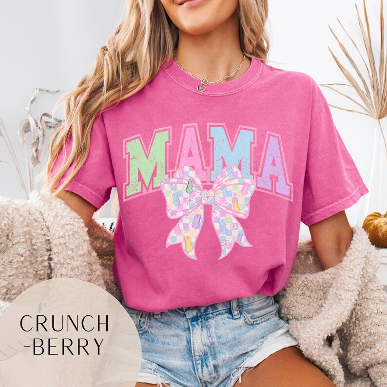 May include: Pink t-shirt with the word "MAMA" in pastel colors and a pastel checkered bow with Easter bunny graphics.