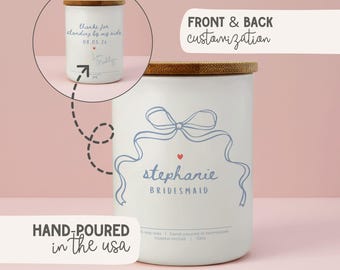 May include: White candle with a wooden lid, featuring a blue ribbon design and the name "Stephanie Bridesmaid." The candle also has the text "Hand-poured in the USA" and "Front & Back customization."