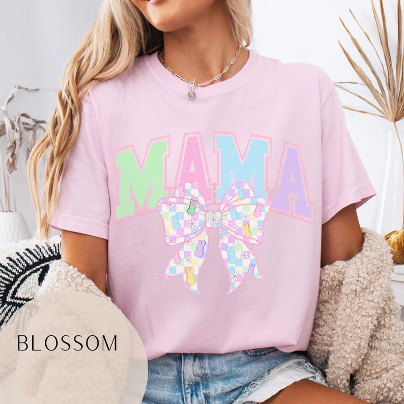 May include: Pink t-shirt with the word "MAMA" in pastel colors and a pastel checkered bow with pastel jelly bean designs.