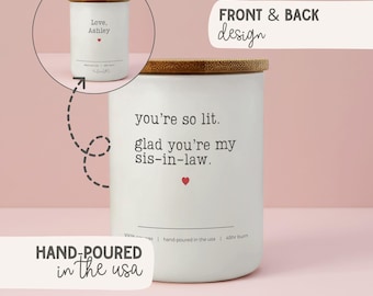 Könnte beinhalten: Weiße Kerze mit Holzdeckel. Auf der Vorderseite der Kerze steht "you're so lit. glad you're my sis-in-law." mit einem roten Herzen. Die Kerze wird in den USA von Hand gegossen und aus Sojawachs hergestellt. Die Kerze hat eine Brenndauer von 40-50 Stunden.