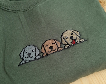 May include: Green sweatshirt featuring an embroidered design of three Labrador puppy faces in gray, brown, and tan. The puppies are smiling with their tongues out. The sweatshirt is made of a soft material.