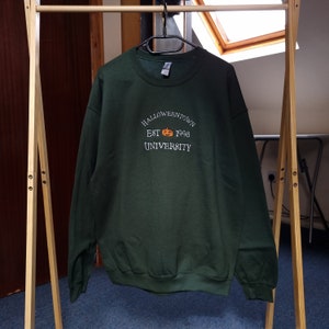 May include: A dark green sweatshirt with the text "HALLOWEENTOWN EST 1998 UNIVERSITY" and a small orange pumpkin graphic.