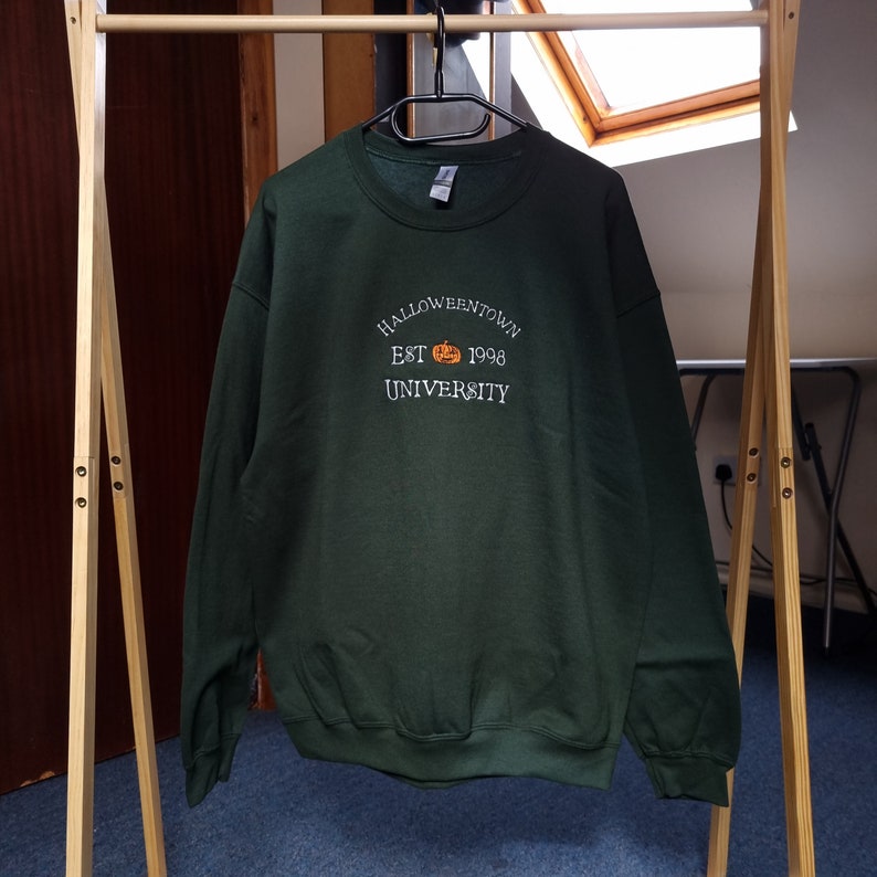 May include: A dark green sweatshirt with the text "HALLOWEENTOWN EST 1998 UNIVERSITY" and a small orange pumpkin graphic.